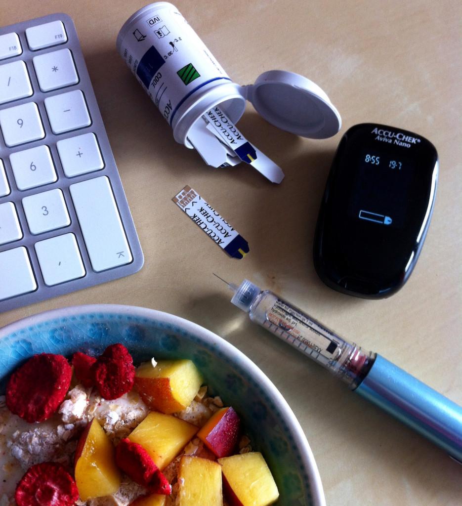 An insulin pen, meter, strips, keyboard, and a bowl of cereal with fruit